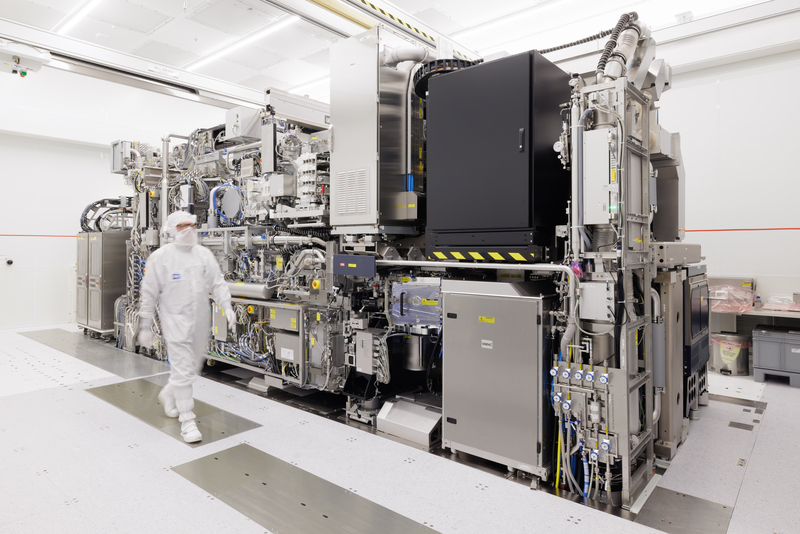 Een medewerker in een wit beschermpak loopt langs een grote ASML NXE:3800E-chipmachine in een cleanroom in Veldhoven.