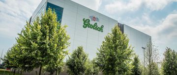 Buitenkant van de Grolsch-brouwerij met het groene logo op de gevel, achter bomen.