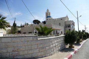 Een straat met een stenen kerk en palmbomen in Taybeh op de Westelijke Jordaanoever, in 2018.