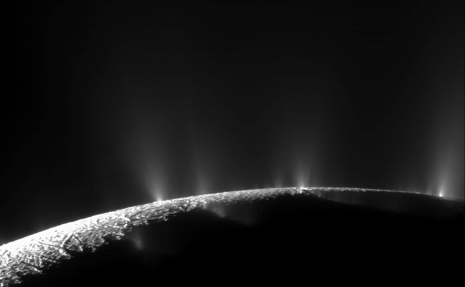 Zwart-witmozaïek van Cassini met pluimen van ijs en waterdamp boven de verlichte rand van Enceladus.