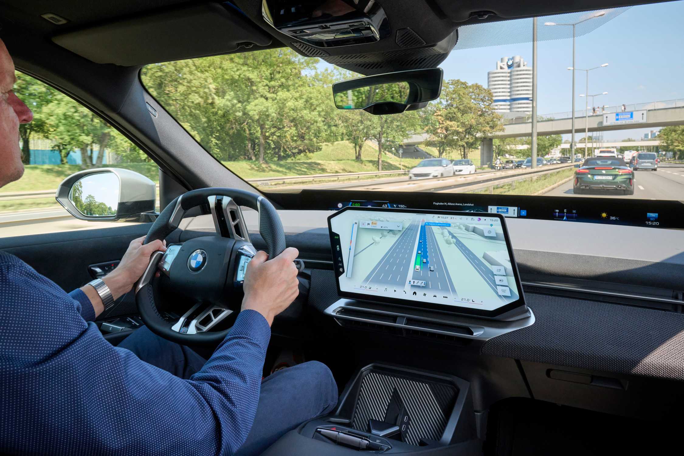 BMW-persfoto: bestuurder met handen aan het stuur, naast het centrale scherm met een 3D-route en weergegeven rijstroken.