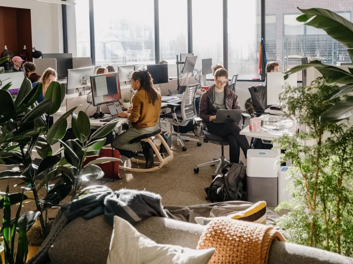 Medewerkers van Anthropic werken aan bureaus tussen grote ramen en planten.