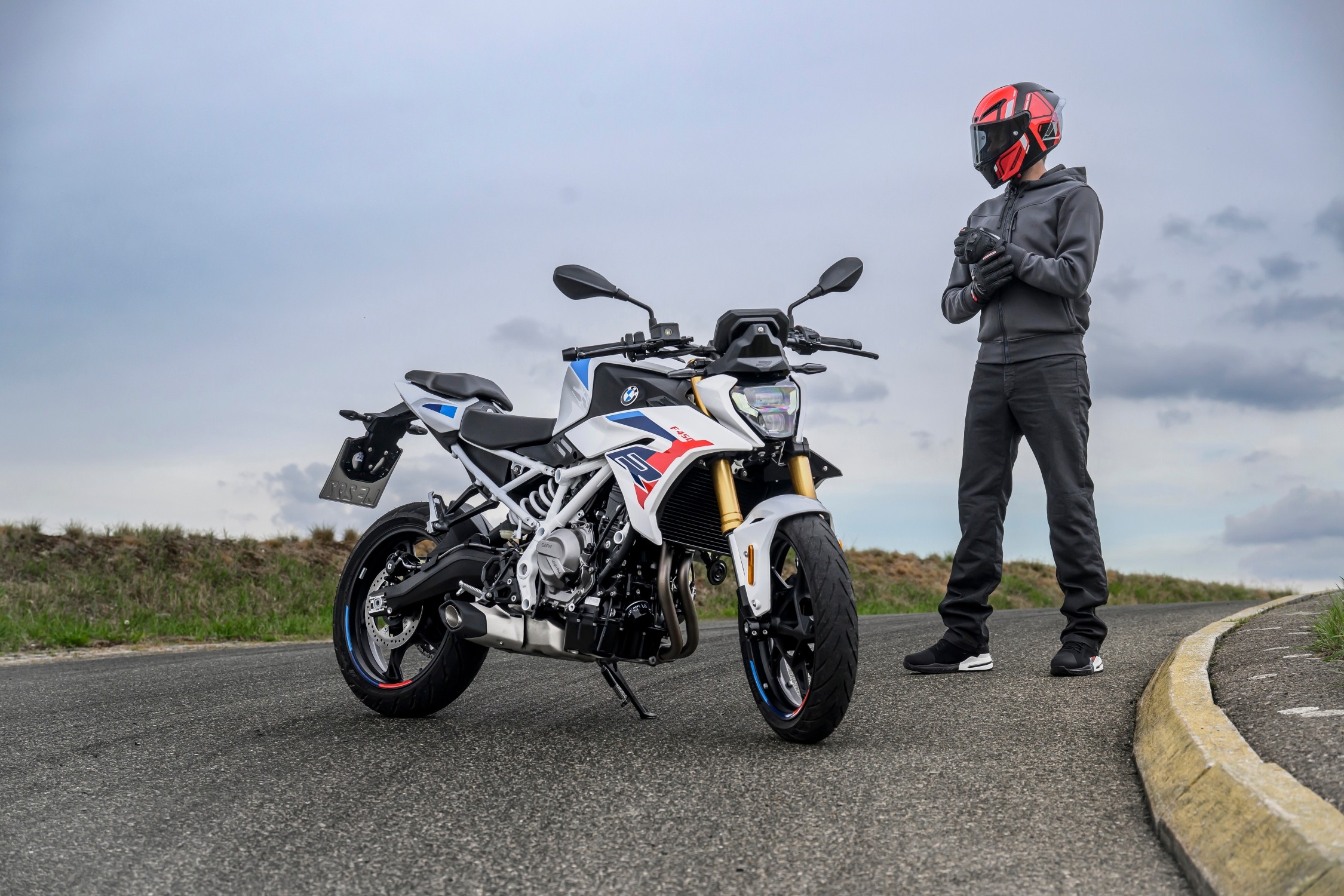 Witte BMW F 450 R met M-kleuren staat op een weg naast een motorrijder in zwarte kleding.