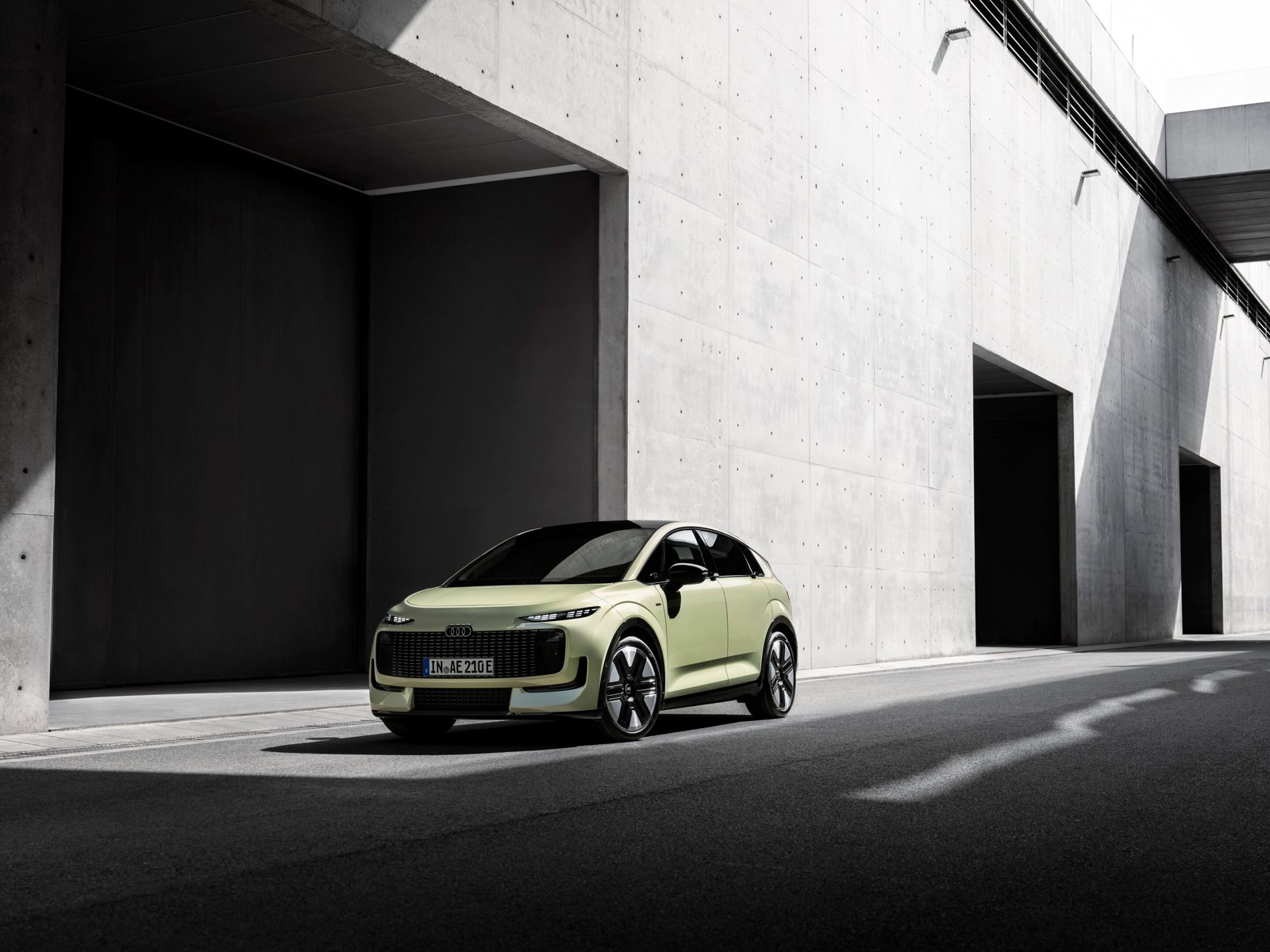 Pistachegroene Audi A2 e-tron van schuin voren, op een straat langs een betonnen gebouw.