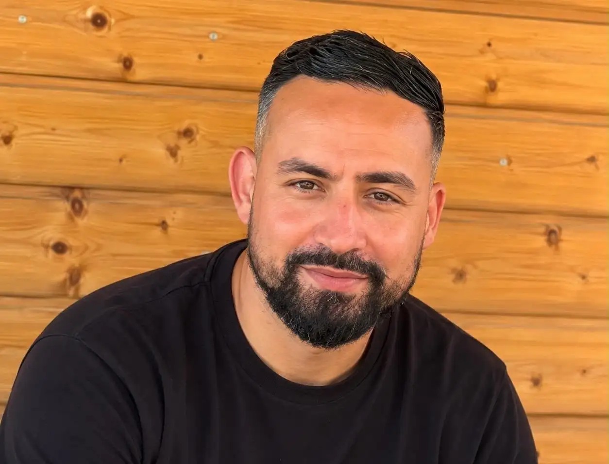 Portret van politieagent Nordine El Talbi, met een zwart shirt voor een houten wand.