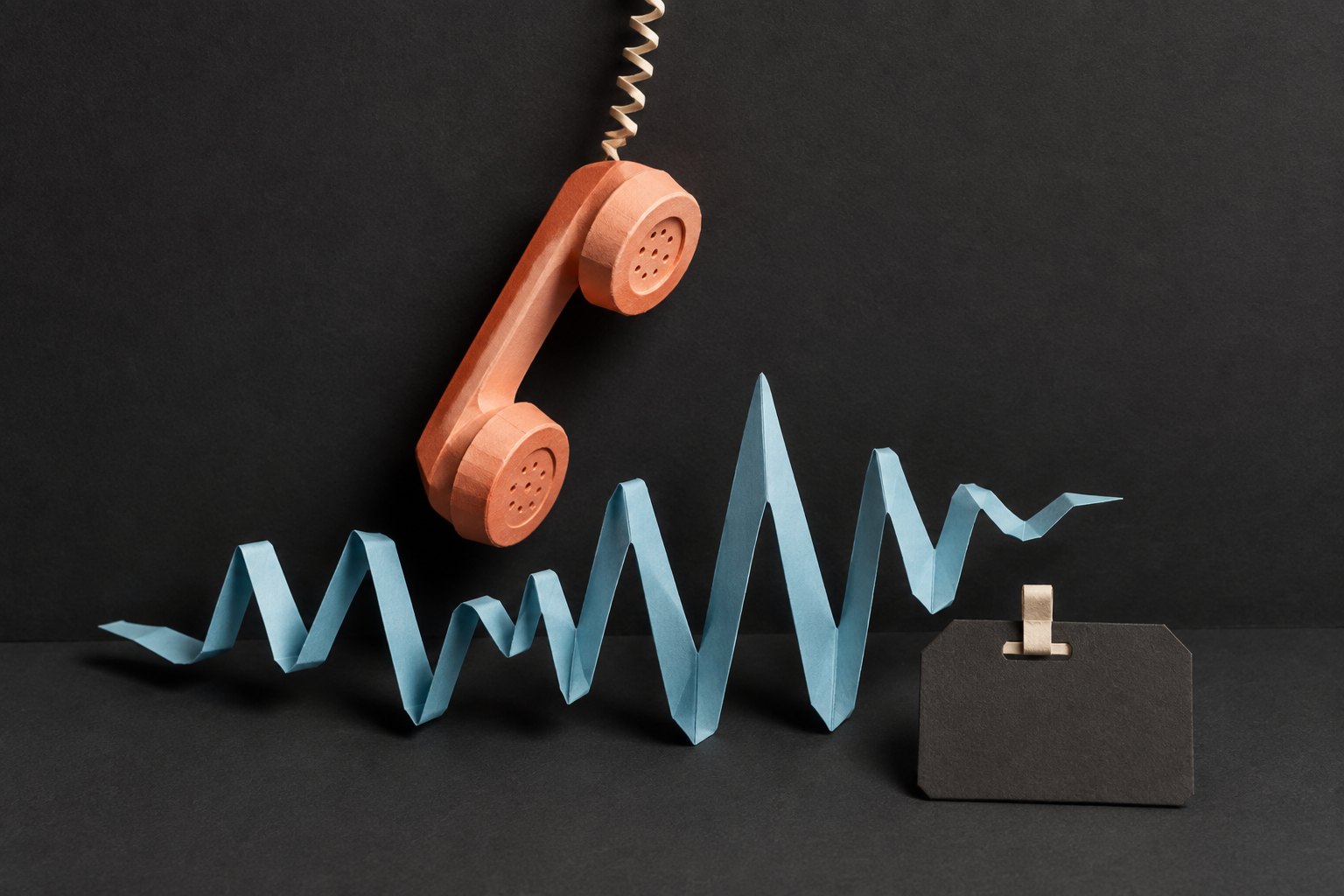 AI-illustratie van een perzikkleurige telefoonhoorn en een gevouwen blauwe geluidsgolf van papier; geen weergave van de echte opname.