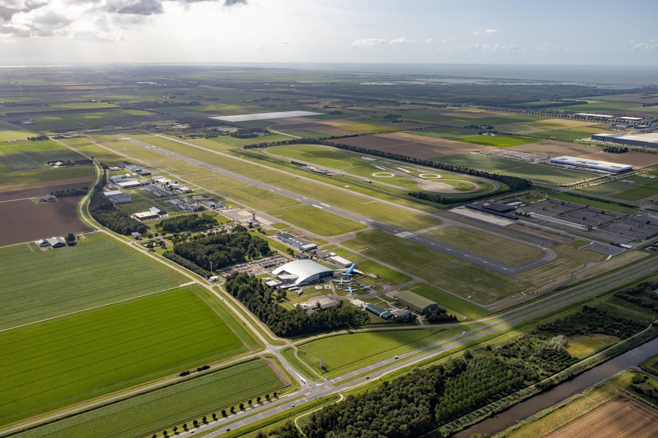 Luchtfoto van Lelystad Airport met de startbaan, luchthavengebouwen en omliggende landbouwgrond.