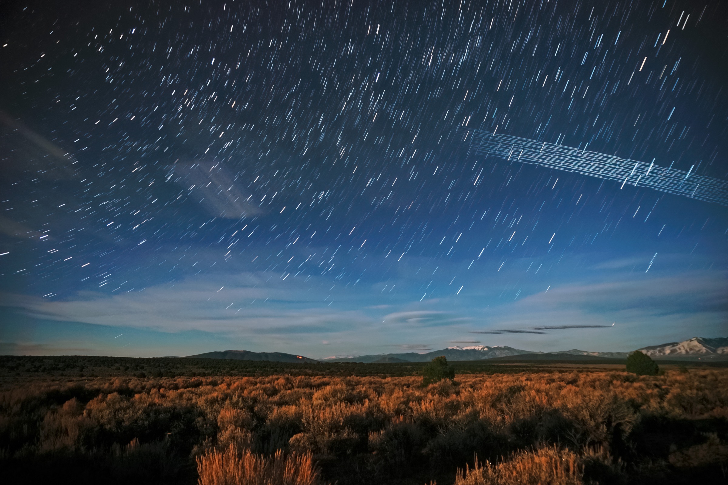 Lichtsporen van Starlink-satellieten en sterren boven een donker landschap bij Carson National Forest in New Mexico.
