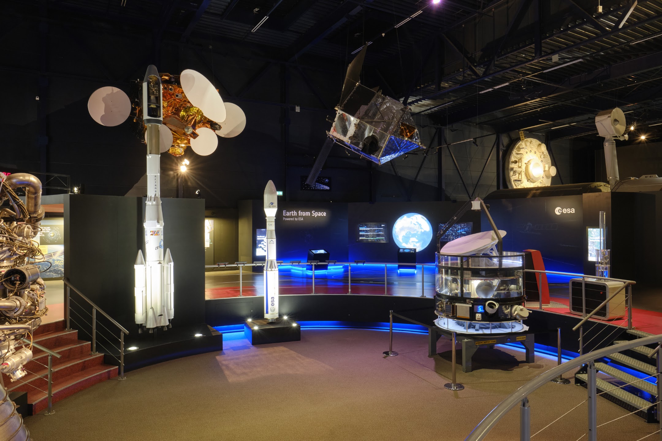 De tentoonstellingsruimte van Space Expo met ruimtevaartobjecten, raketmodellen en blauwe verlichting; de Pokémon-speurtocht is niet afgebeeld.