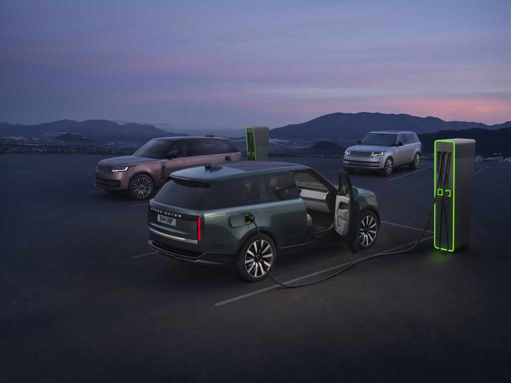 Range Rover Electric-modellen naast laadpunten bij schemering, met bergen op de achtergrond. Origineel persbeeld van JLR.
